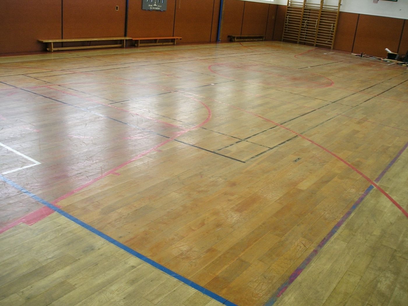 Vybledlá a poškrábaná palubovka tělocvičny před renovací
